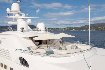 A luxurious yacht with a hot tub and sun loungers is anchored in a calm bay with a picturesque coastline.