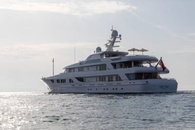 The luxurious yacht Nectar cruises through sparkling waters under a bright, hazy sky.