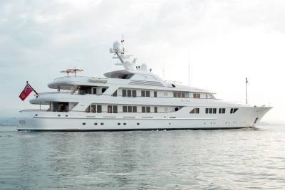 The luxurious white yacht Nectar glides gracefully across the calm, shimmering water under a bright sky.