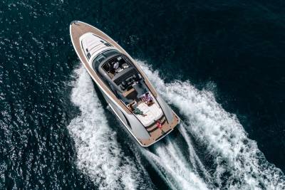 A sleek yacht glides through dark blue waters, leaving a foamy wake as passengers relax on deck.