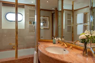 Luxurious gold fixtures and marble countertops adorn this elegant yacht bathroom with a porthole view.