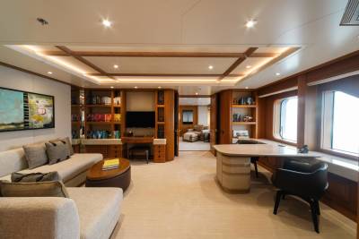 A luxurious yacht interior features a comfortable living area with a sofa, bookshelves, and a dedicated workspace by the window.