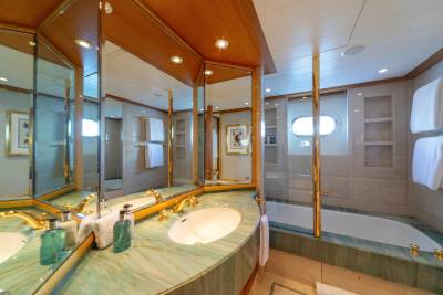 Luxurious yacht bathroom features a green marble vanity, gold fixtures, and a deep soaking tub with an oval porthole.