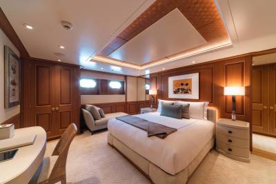 Luxurious yacht stateroom features warm wood paneling, a plush king-size bed, and elegant, modern furnishings.