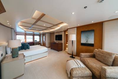 Luxurious yacht stateroom features a plush bed, seating area, and panoramic windows overlooking the water.