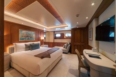 Luxurious yacht cabin features a king-sized bed, elegant wood paneling, and a private desk area.