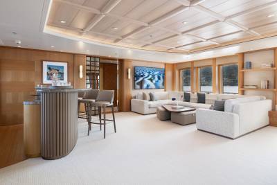 This elegant yacht lounge features a sophisticated bar, plush seating, and a large screen displaying a stunning desert landscape.