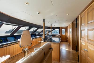 The luxurious bridge of a yacht offers panoramic views of a rocky coastline bathed in soft sunlight.