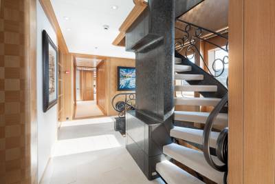 A luxurious spiral staircase with ornate railings ascends through a bright, wood-paneled hallway adorned with artwork.