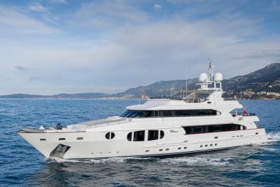 A luxurious white yacht cruises through the azure waters off a picturesque coastal town nestled against rolling hills.