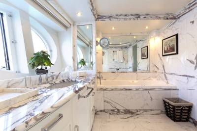 Luxurious marble adorns this elegant bathroom, featuring a deep soaking tub and a spacious vanity with a large window.