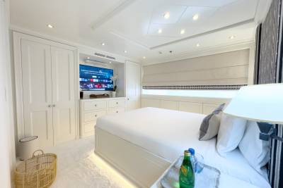 A luxurious yacht cabin features a comfortable bed, integrated entertainment system, and elegant built-in cabinetry.