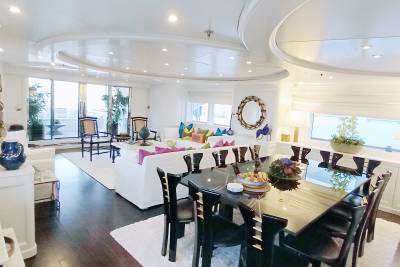 A spacious yacht salon offers a luxurious dining area and a comfortable lounge with large windows overlooking the water.