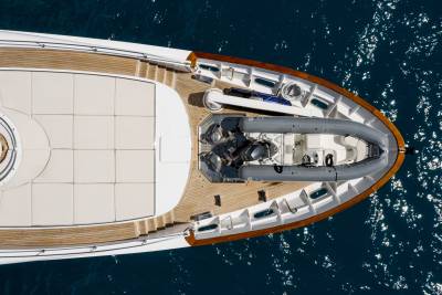 An aerial view reveals the sleek deck of a luxury yacht with a tender boat secured at its bow, floating on the deep blue sea.
