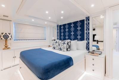 Luxurious blue and white bedding adorns a spacious yacht cabin with nautical-themed accents and ample storage.