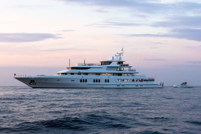 A luxurious white superyacht named Coral Ocean glides across calm waters under a soft, pastel sky.