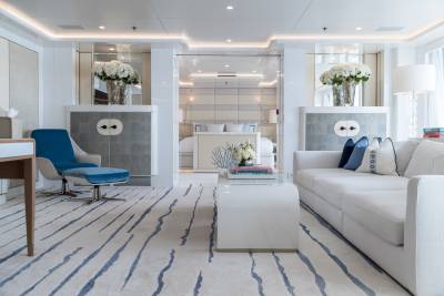A luxurious yacht interior features a plush white sofa, a striking blue armchair, and a modern coffee table in a serene, light-filled living area.