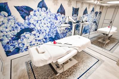 A luxurious spa room features a massage bed adorned with a single red rose against a stunning floral mosaic wall.
