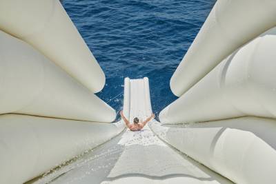 A person slides down an inflatable water slide into the blue ocean.
