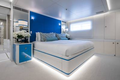 A luxurious yacht cabin features a striking blue headboard, plush white bedding, and ambient under-bed lighting.