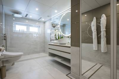 Luxurious white robes hang in a modern, marble-clad bathroom with a sleek vanity and a large circular mirror.
