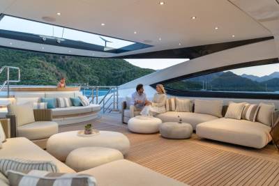 A couple enjoys a serene conversation on a luxurious yacht deck overlooking a picturesque mountainous coastline.