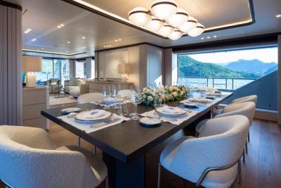 A beautifully set dining table on a yacht offers a stunning view of a mountainous coastline.
