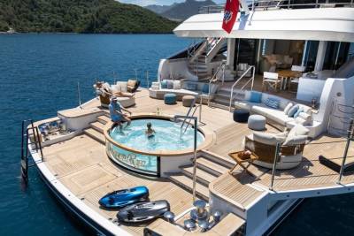 A luxurious yacht offers a refreshing dip in its jacuzzi and ample lounging space amidst a stunning coastal backdrop.