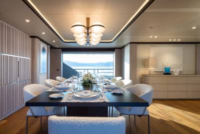 An elegant dining room aboard a yacht offers a stunning view of the sea and distant mountains.