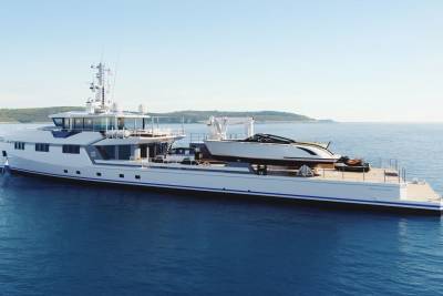 A sleek support yacht carries a smaller tender and jet skis across the calm blue ocean.