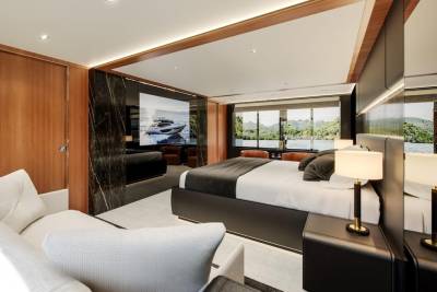 Luxurious yacht interior features a spacious bedroom with a large screen displaying a yacht and stunning water views.