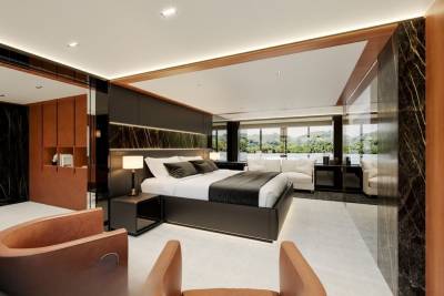 Luxurious modern bedroom with a king-size bed, marble accents, and panoramic windows overlooking a lush green landscape.