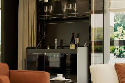 A modern home bar with wine glasses and a bottle of wine is showcased next to a window with a view of lush greenery.