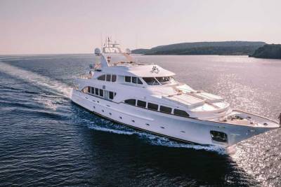 A luxurious white yacht glides through the sparkling blue waters, leaving a trail of white foam in its wake.