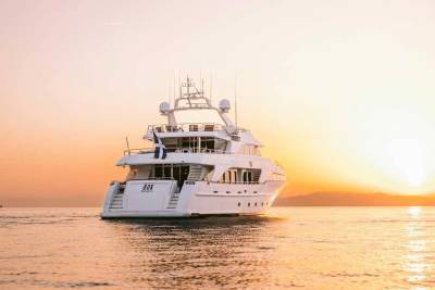 A luxurious yacht sails on calm waters at sunset, with the sun casting a warm glow over the horizon.