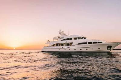 A luxurious white yacht glides across calm waters at sunset, silhouetted against a soft pink and orange sky.