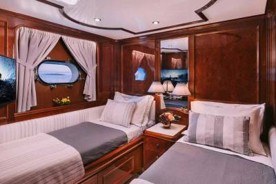 Luxurious twin beds with plush pillows and striped throws are perfectly situated in this elegant wood-paneled cabin with a porthole view.