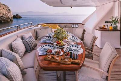 A beautifully set dining table awaits on a yacht deck, overlooking a serene coastal landscape.