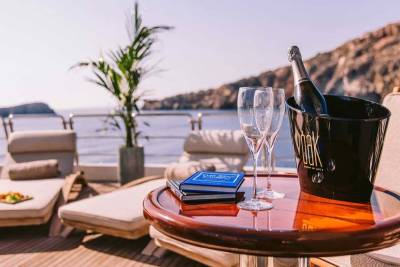 Champagne chills in an ice bucket on a yacht deck, ready to be enjoyed with two glasses and a scenic coastal view.