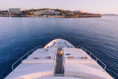 Cruising on a luxurious yacht towards a picturesque coastal resort bathed in golden hour light.