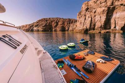 A luxury yacht anchors in a secluded cove, ready for a day of water sports with tubes, skis, and dive gear.