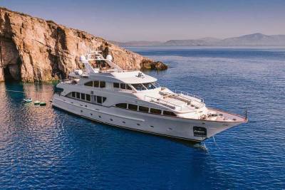 A luxurious white yacht rests peacefully in a secluded cove beside a dramatic, rocky coastline.