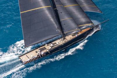 A sleek black yacht with striking yellow accents cuts through the vibrant blue ocean, its sails full and crew at the ready.