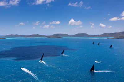 Black-sailed yachts race across the turquoise waters of the British Virgin Islands under a brilliant blue sky.