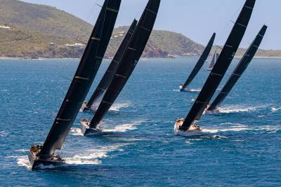 Sleek black sails dominate the azure waters as racing yachts vie for position under a clear blue sky.