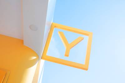 A bright yellow "Y" sign is framed by a modern architectural structure against a clear blue sky.