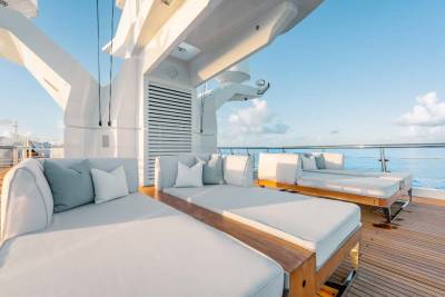 A spacious and modern outdoor deck area on a cruise ship, featuring comfortable lounge chairs and sofas with a view of the ocean in the background.