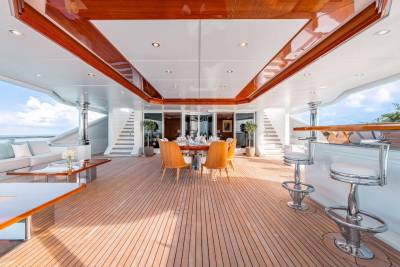 A luxurious yacht interior with a spacious deck, wooden floors, and a dining area with orange chairs, surrounded by a scenic ocean view.