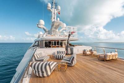 A luxurious yacht with a spacious deck, featuring striped cushions and lounge chairs, set against a backdrop of a serene ocean and cloudy sky.