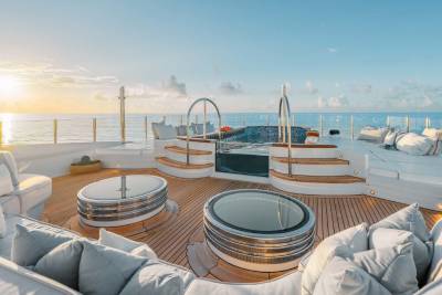 A luxurious yacht deck with comfortable seating areas, a glass-enclosed dining space, and a stunning view of the ocean at sunset.